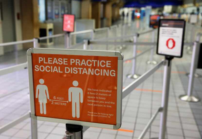 A sign reminds people to practice social distancing in the security checkpoint line at DFW...