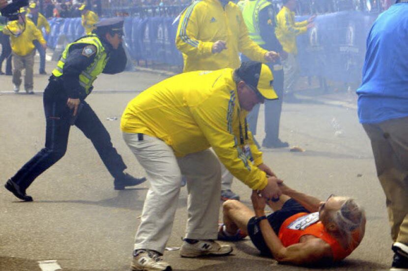 A race official assists Bill Iffrig, 78, after the first explosion at the Boston Marathon.