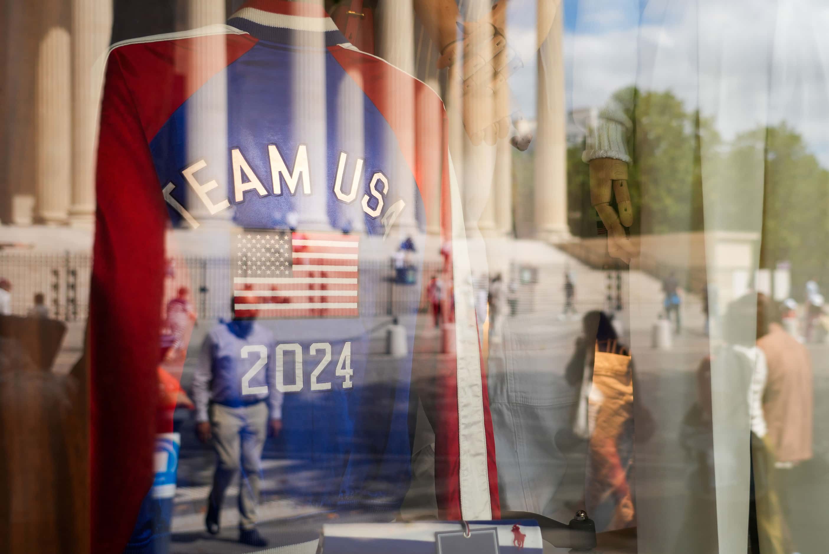 Pedestrians are reflected in the windows of a Ralph Lauren store displaying an Team USA...