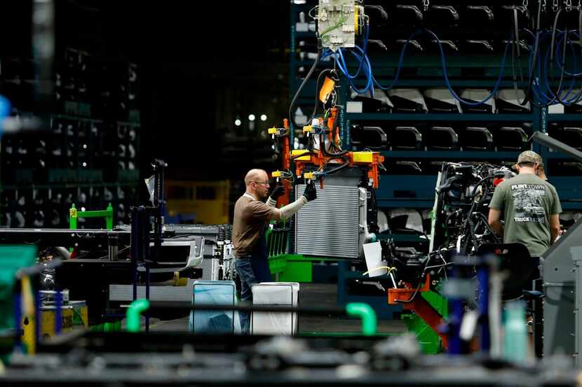 Line workers work on the chassis of full-size General Motors pickups at the Flint Assembly...