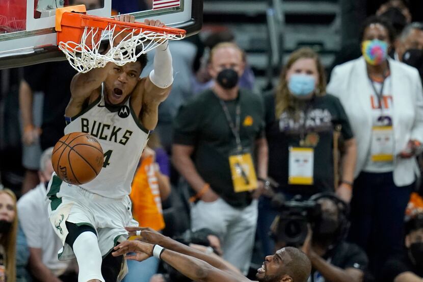 Milwaukee Bucks forward Giannis Antetokounmpo, top, dunks over Phoenix Suns guard Chris Paul...