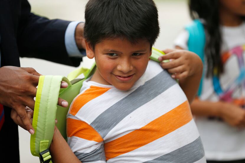 Apolinar Lopez, 8, tries on a new backpack from Adan Gonzalez, third-grade teacher at Bowie...