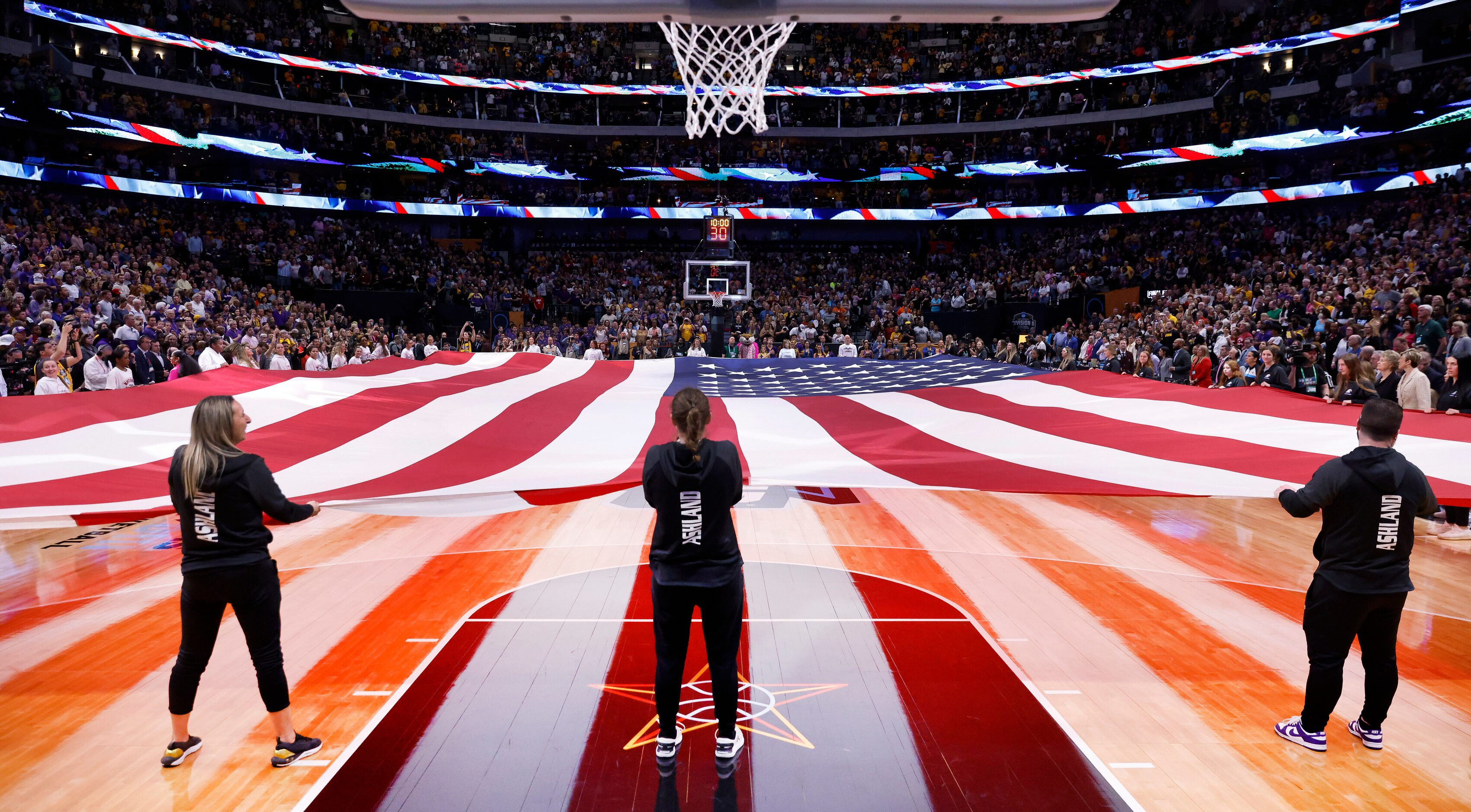 A court-sized U.S. flag is held taught for the national anthem before the NCAA Women’s...