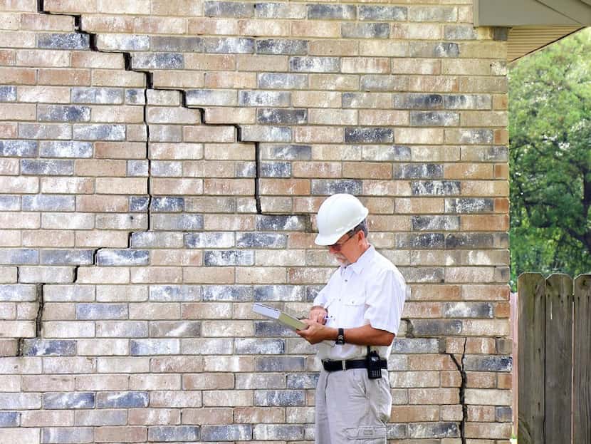 Man in white hard hat in front of brick wall with stairstep crack