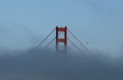 A small plane files past a tower of the Golden Gate Bridge partially covered by fog in San...
