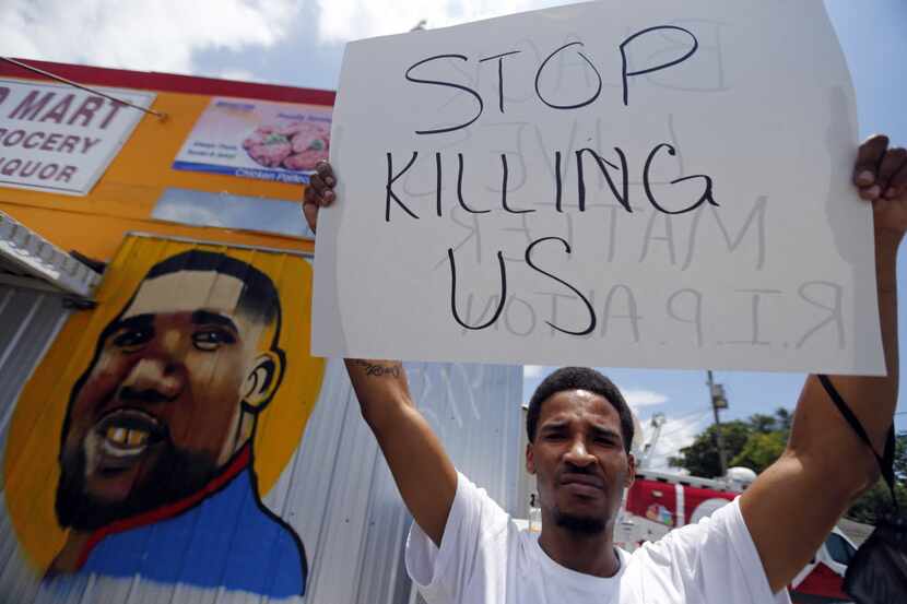 A man holds a sign in front of a mural of Alton Sterling while attorneys, not pictured,...