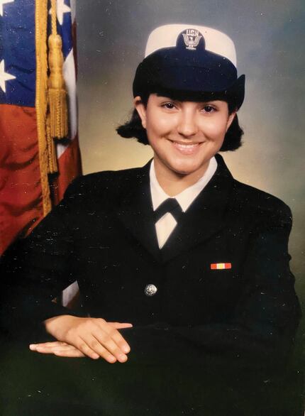 A photo of young Jennifer Sustarich smiling in her Navy uniform in front of the American flag.