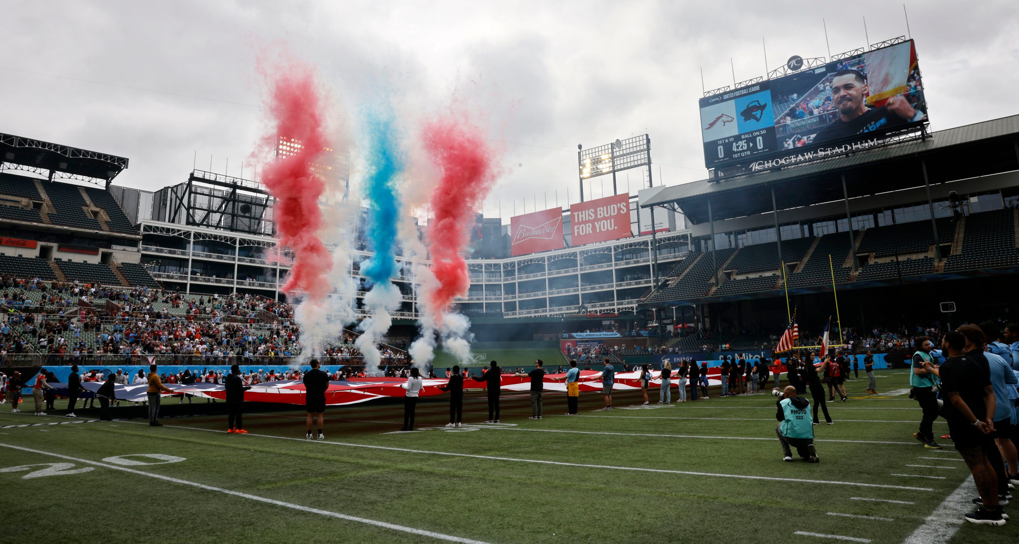 People hold a giant flag during the national anthem before a football game between the...