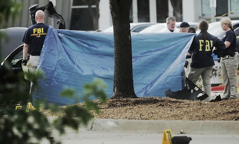 A tarp shields the view Monday morning of the car driven by two men killed Sunday in Garland...