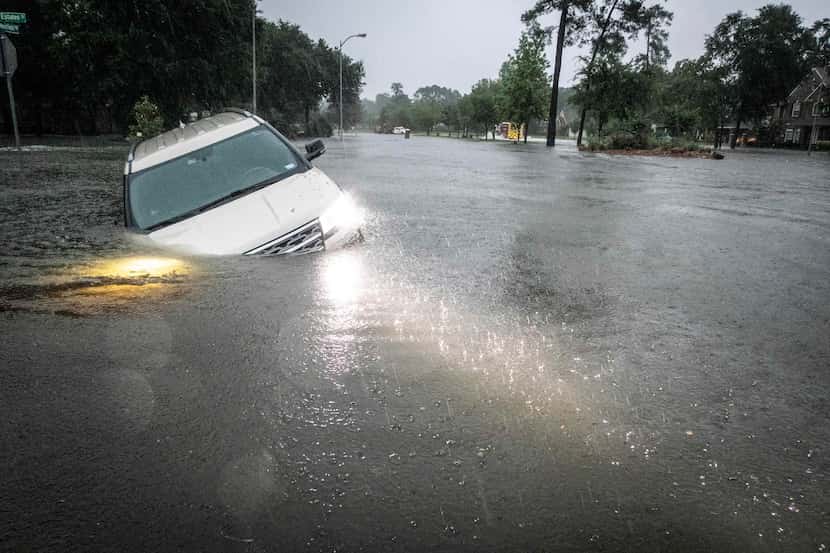 An SUV is stranded in a ditch in a stretch of street flooding during a severe storm,...