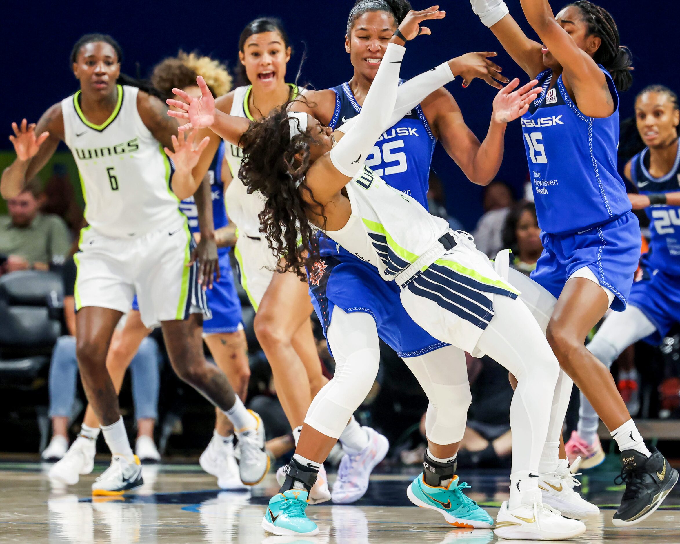 Dallas Wings guard Arike Ogunbowale (24, center) falls backward from the force of throwing...