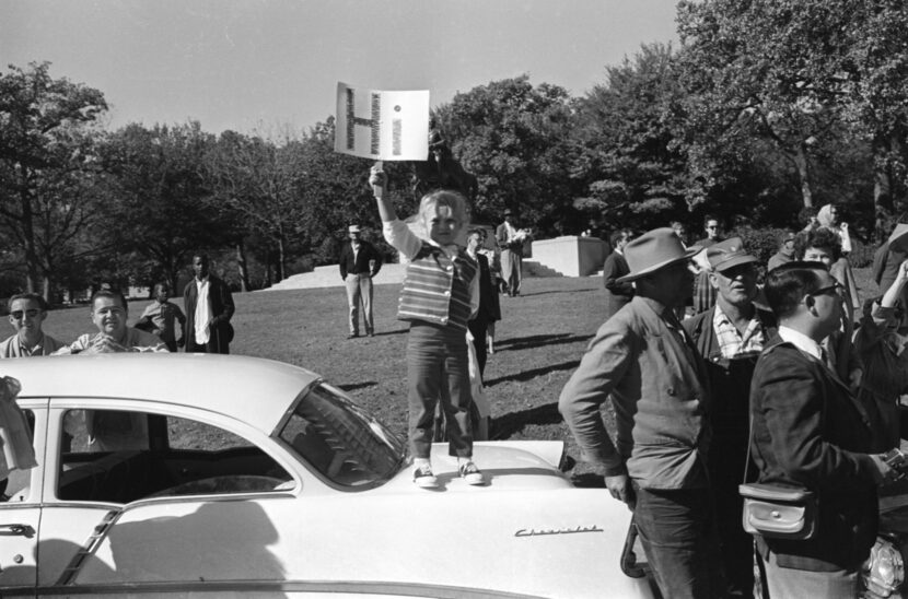 A child holds a sign saying, "Hi" while waiting for Pres. John F. Kennedy's motorcade to...