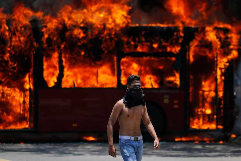 An anti-government protester walks near a bus that was set on fire by opponents of...