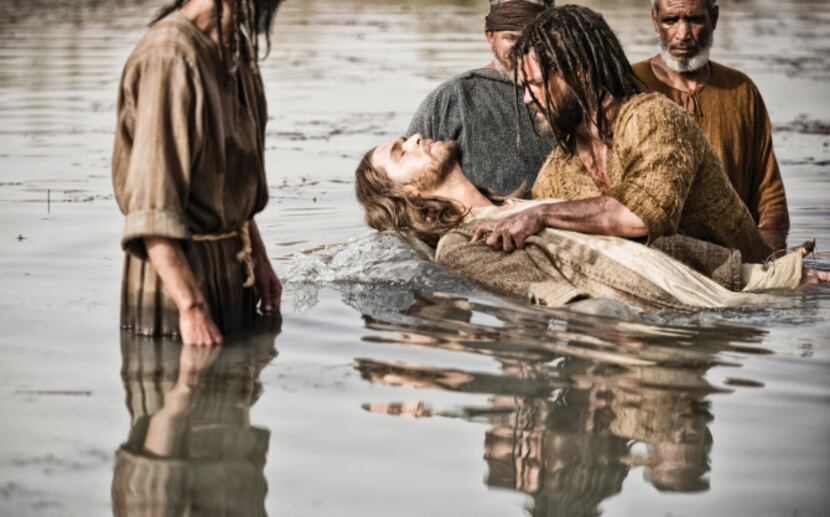Diogo Morcaldo (center) as Jesus is baptized by Daniel Percival, as John, in a scene from...