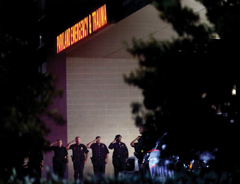 Dallas police officers saluted as vans carrying fallen colleagues exited, presumably to be...