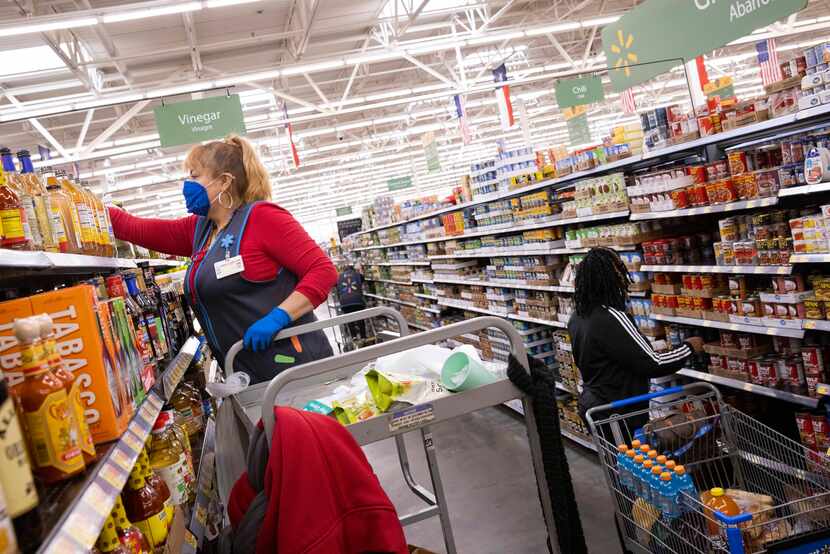 Shoppers shop as Maria Rios (left) stocks shelves at the Walmart at 200 Short Blvd. in Dallas. 