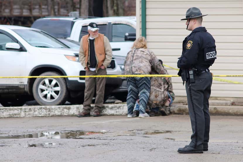 An officer stands guard as people comfort each other near the scene of a fatal shooting at a...