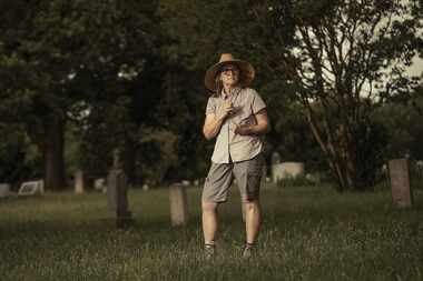 woman in work clothes and wide-brimmed hat surveys a cemetery