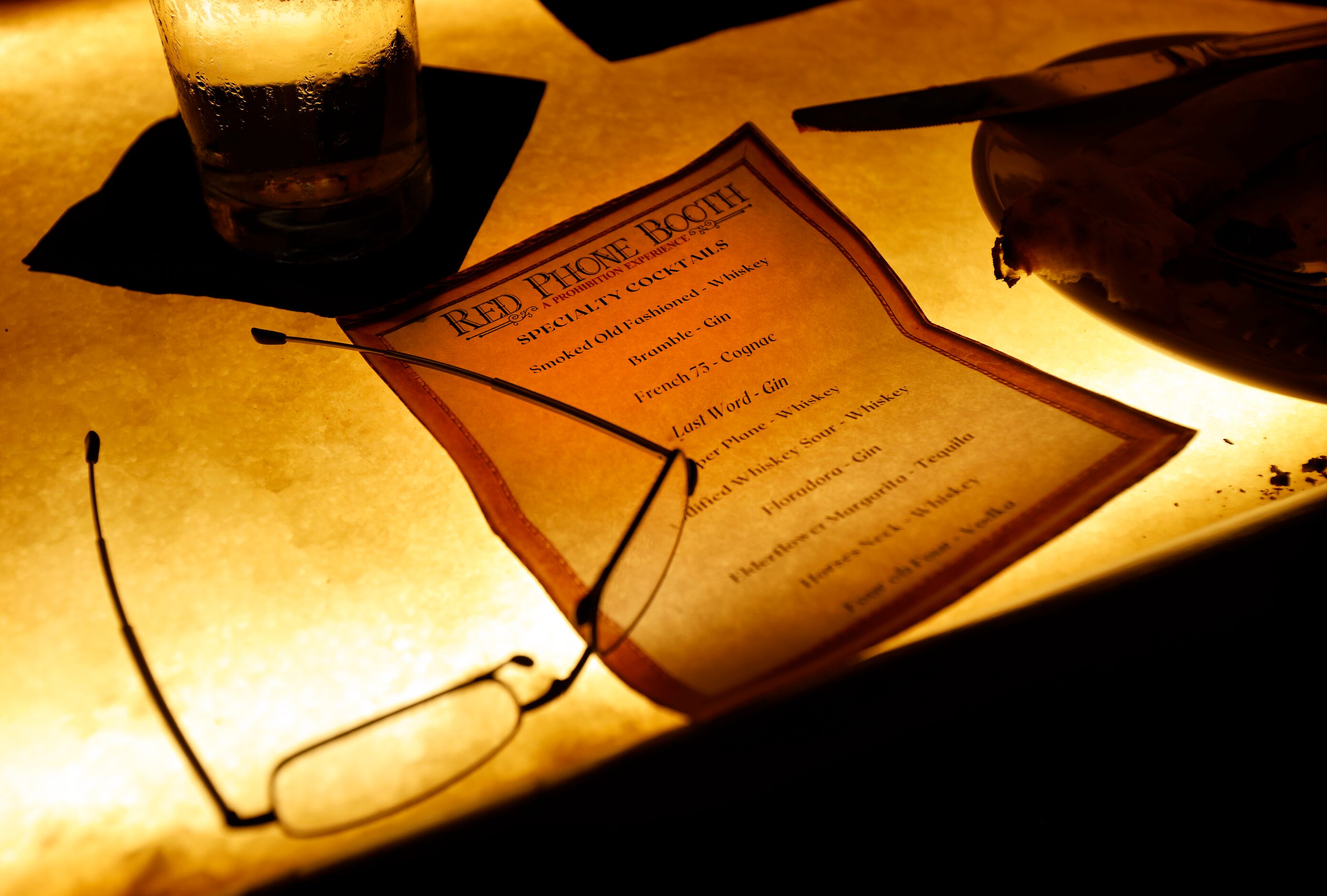 A specialty cocktail menu is illuminated on the backlit bar of Red Phone Booth, a speakeasy...