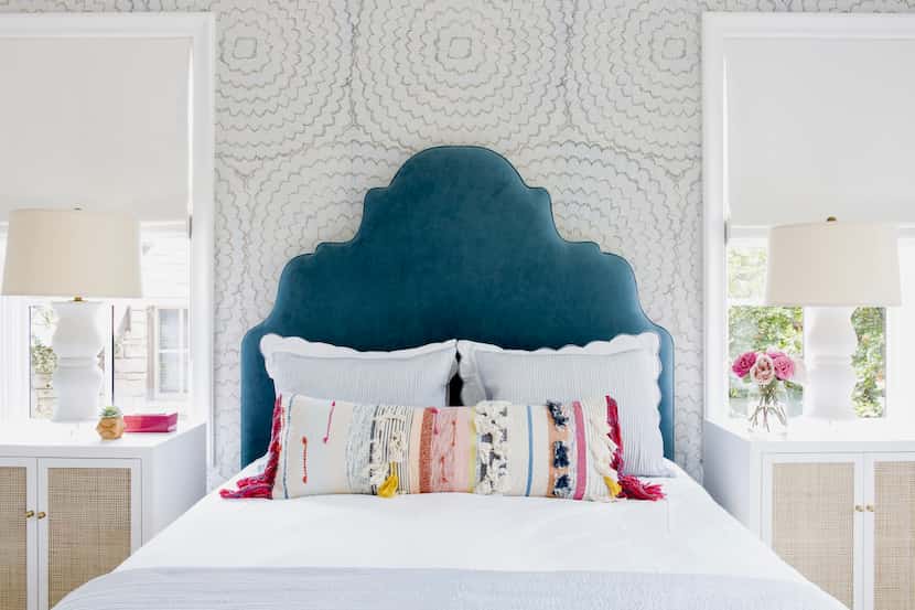 A blue velvet headboard is styled with white sheets and colorful pillows.