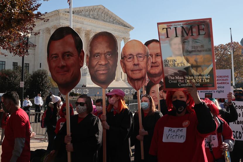 Demonstrators carry photo cut-outs of Supreme Court justices during arguments in Dobbs v....