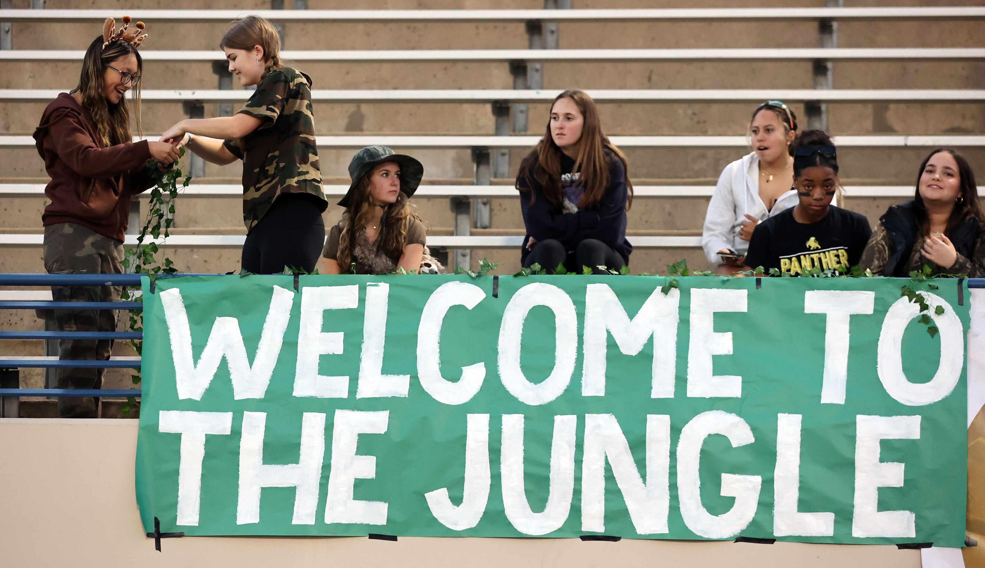 Two Plano East student fans add foliage to the jungle before the first half of a high school...