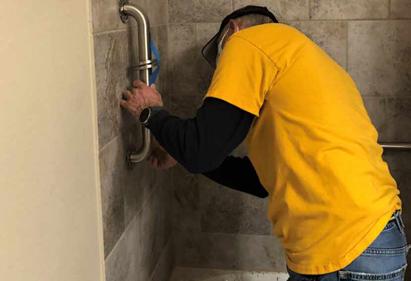 A volunteer in a yellow shirt installs a shower grab bar.