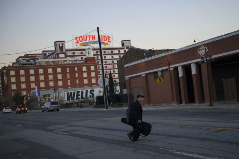 A musician crosses Lamar St. with his guitars in the South Side area of The Cedars.