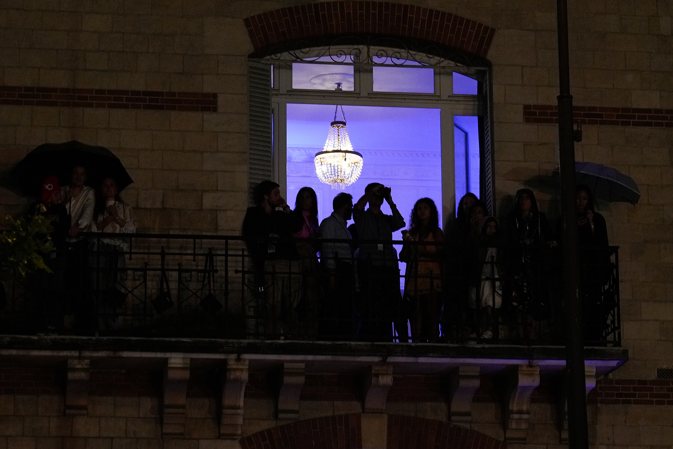 People watch from the balcony of a building along the Seine during opening ceremonies for...