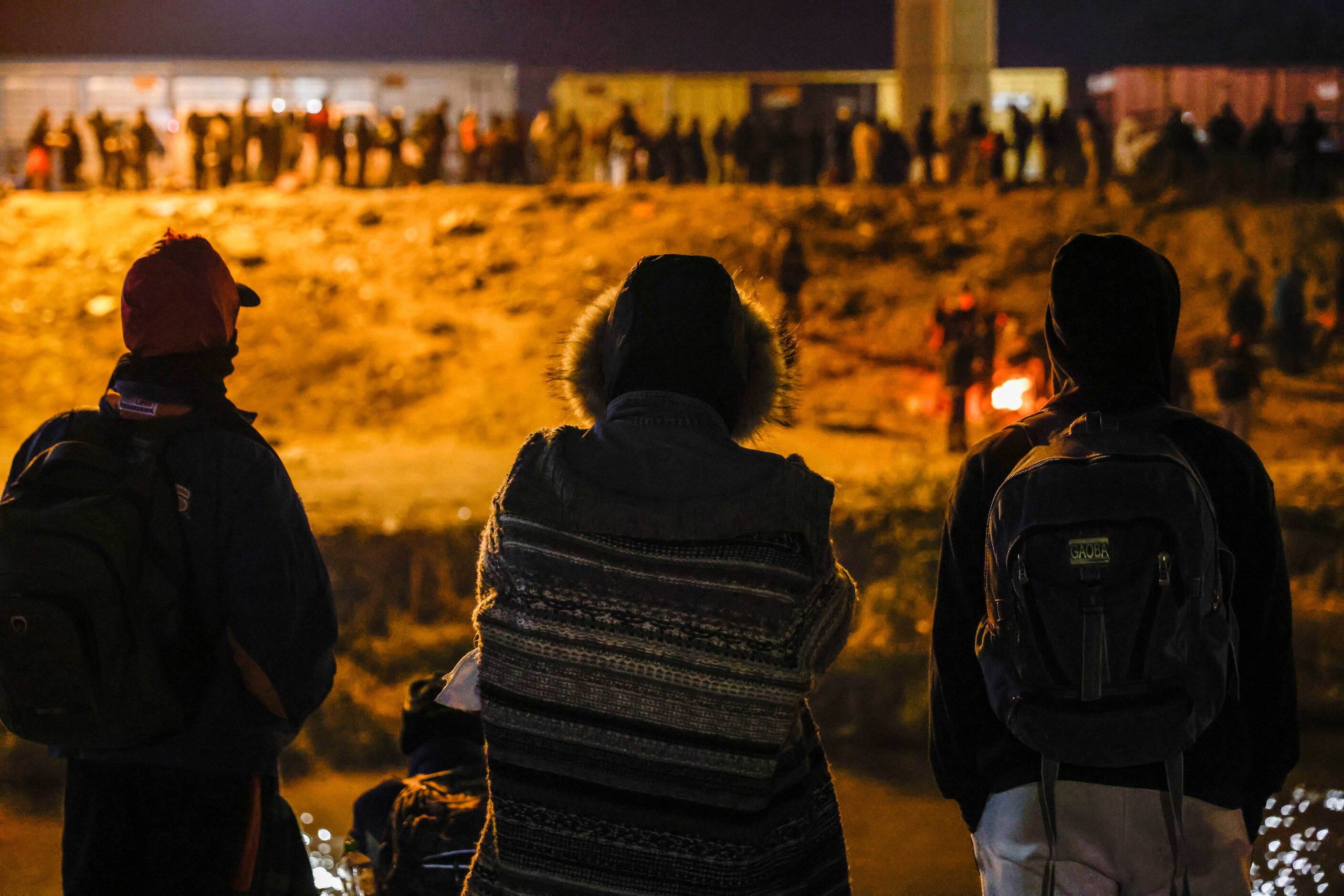 A group of migrants from Venezuela observe the line of other migrants along a border wall in...