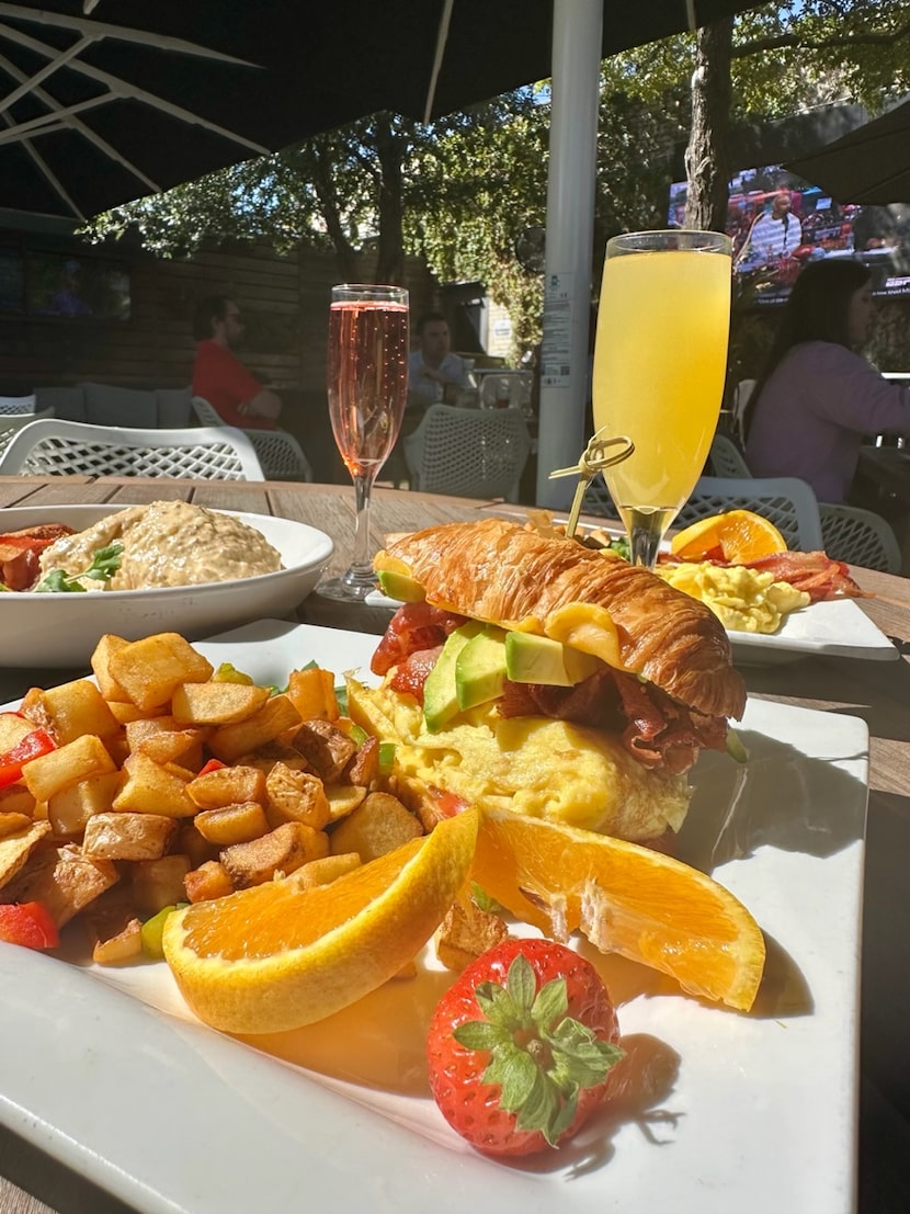 A breakfast sandwich with a croissant has a side of potatoes.