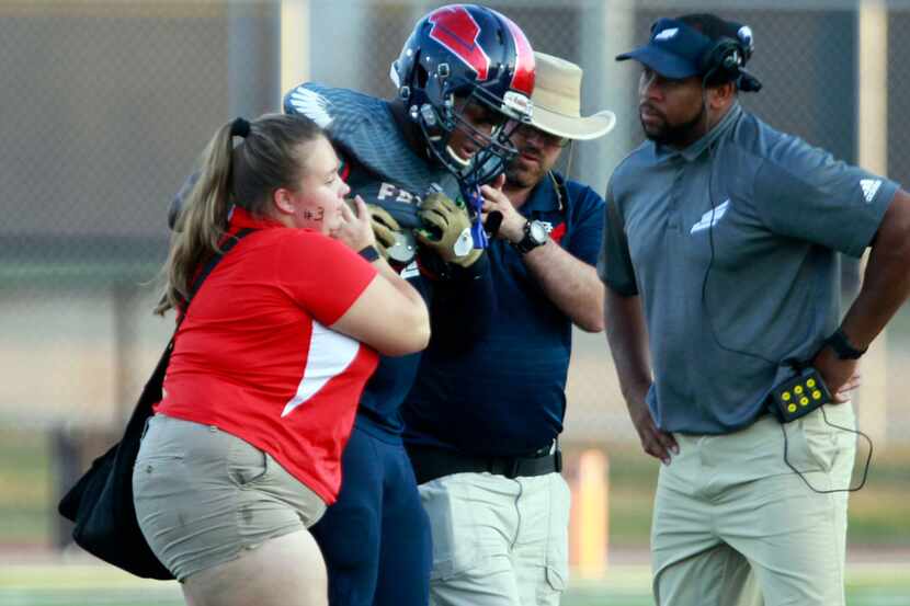 Trainers and coaches help Bishop Dunne linebacker Brennon Scott from the field after he was...
