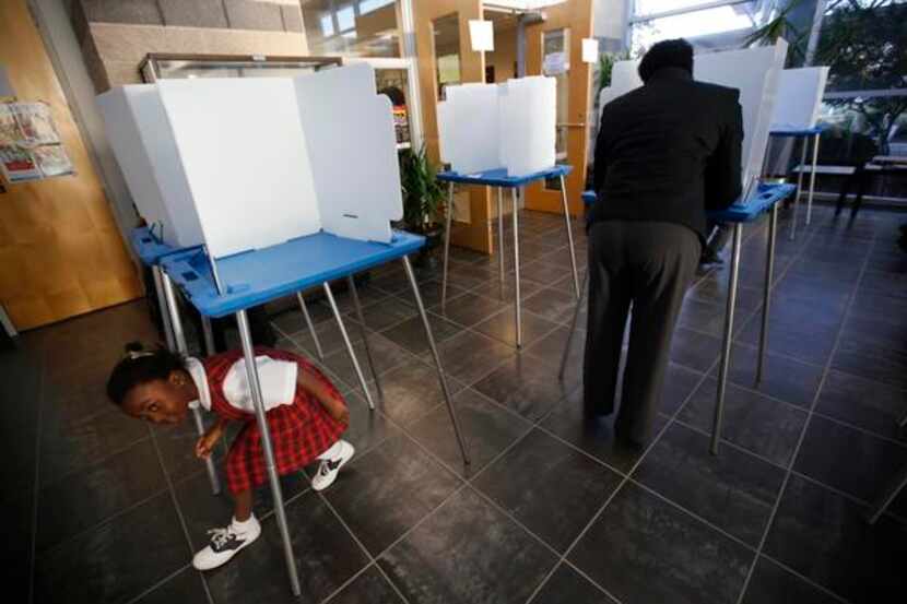 
Christiana Adesanya, 6, plays around voting area while her mother Christine Adesanya,...