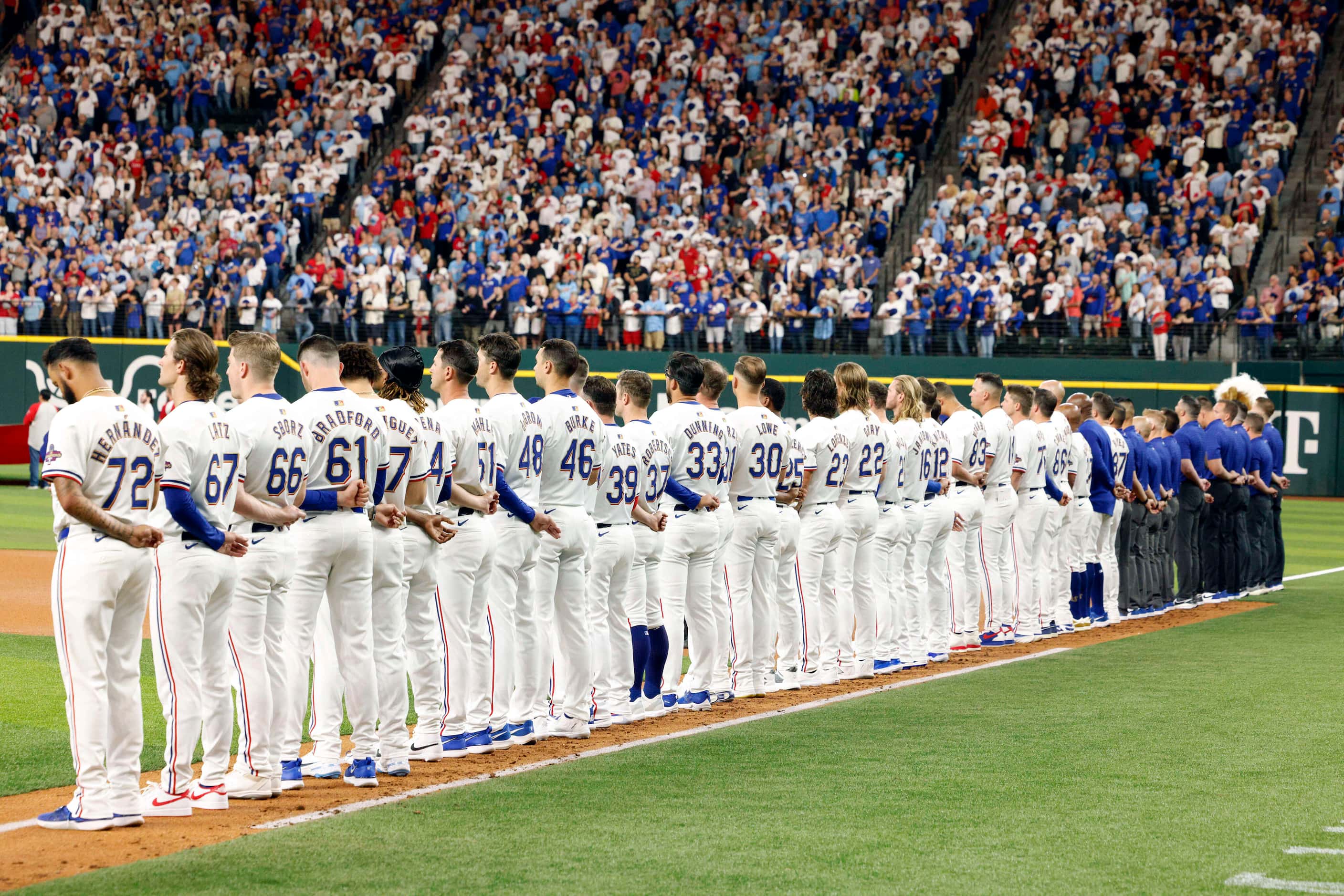 Members of the Texas Rangers stand for the national anthem before the season opener against...