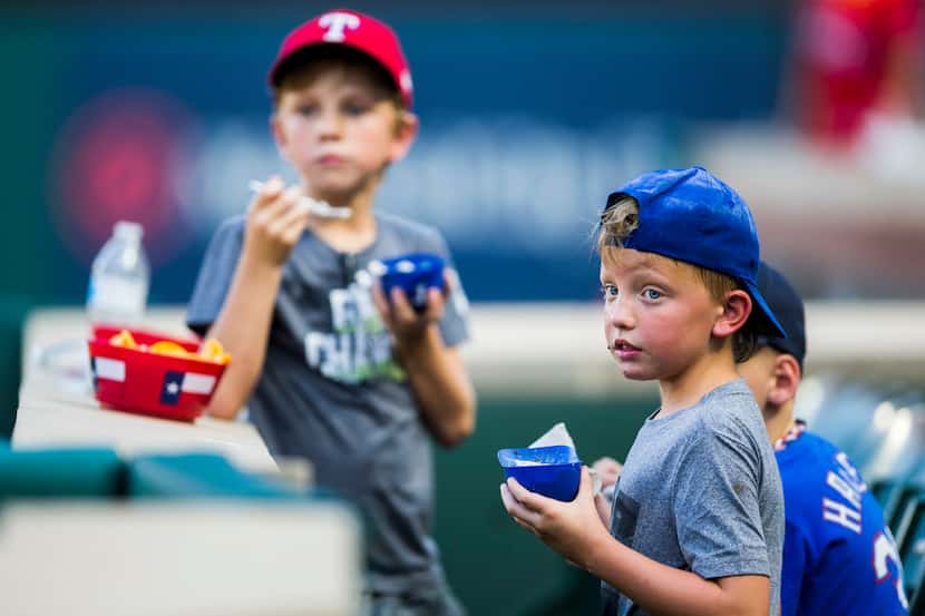 Boys eat ice cream out of mini batting helmets before an MLB game between the Texas Rangers...