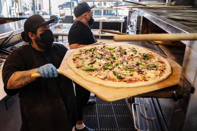 Juan Delgado, left, loads a veggie pizza into the oven while working alongside pizza maker...