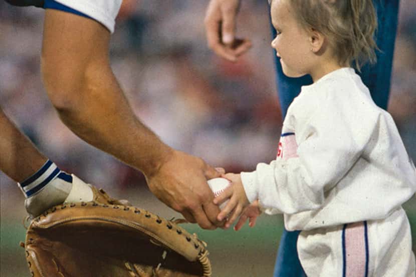  April 4, 1988--Two-year-old Jessica McClure gets the baseball from Texas Rangers catcher...