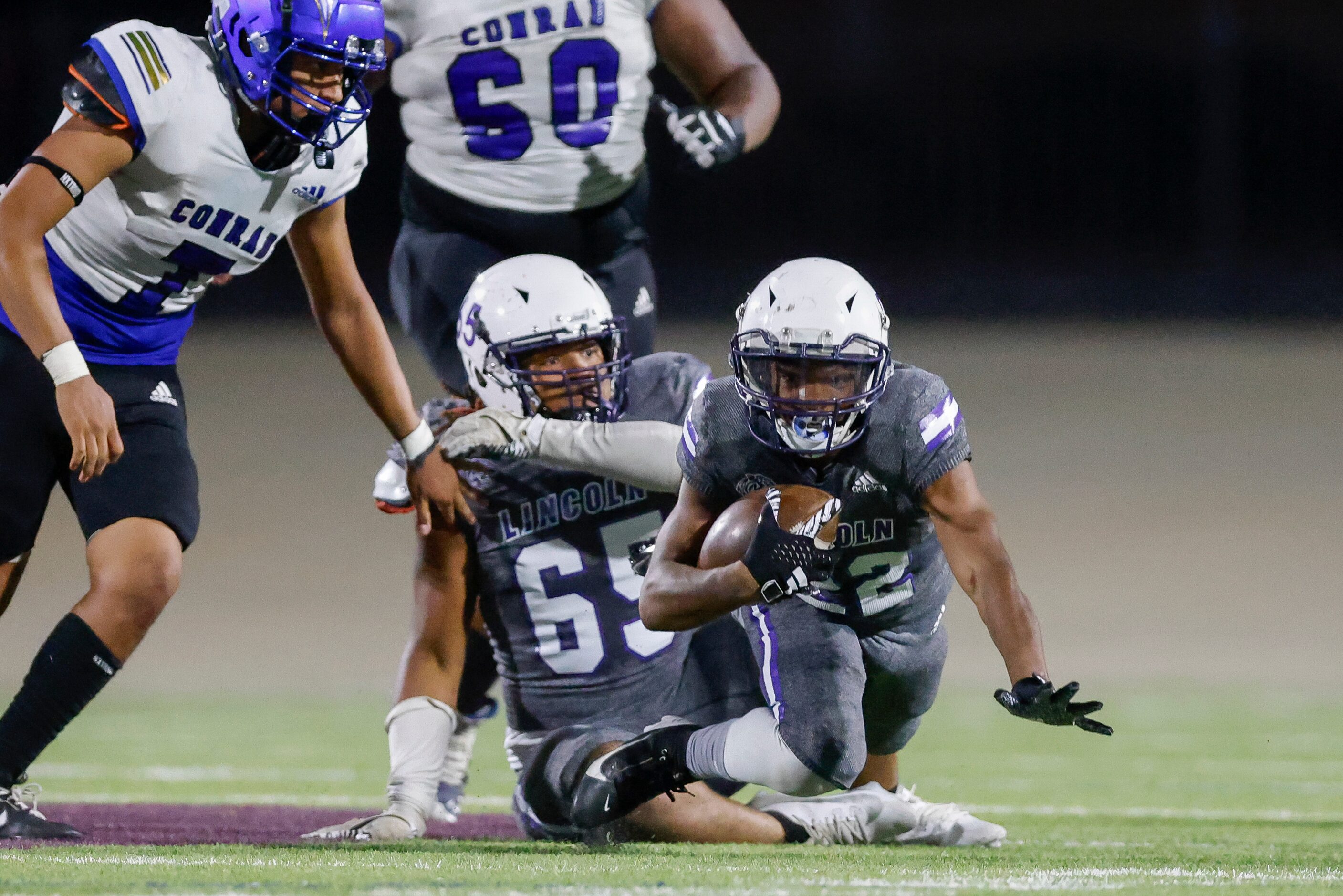 Lincoln running back Demarcus Sypho (22) trips over offensive lineman Kaiden Scott (65)...