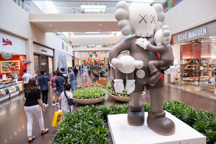 Shoppers walk by KAWS' "CLEAN SLATE" at NorthPark Center. The mall is trying to help both...