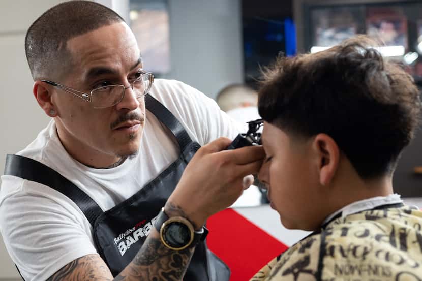 Barber Edgar "E" Montelongo, 35, uses a trimmer to cut the hair of Nathan Cabrera, 12, as he...