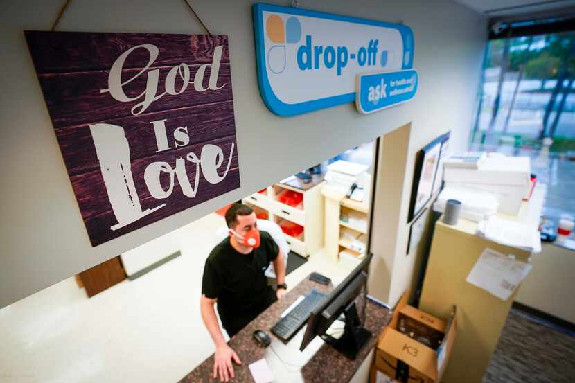 A sign above the window reads "God is Love" as pharmacist Carlos Irula works at a computer...