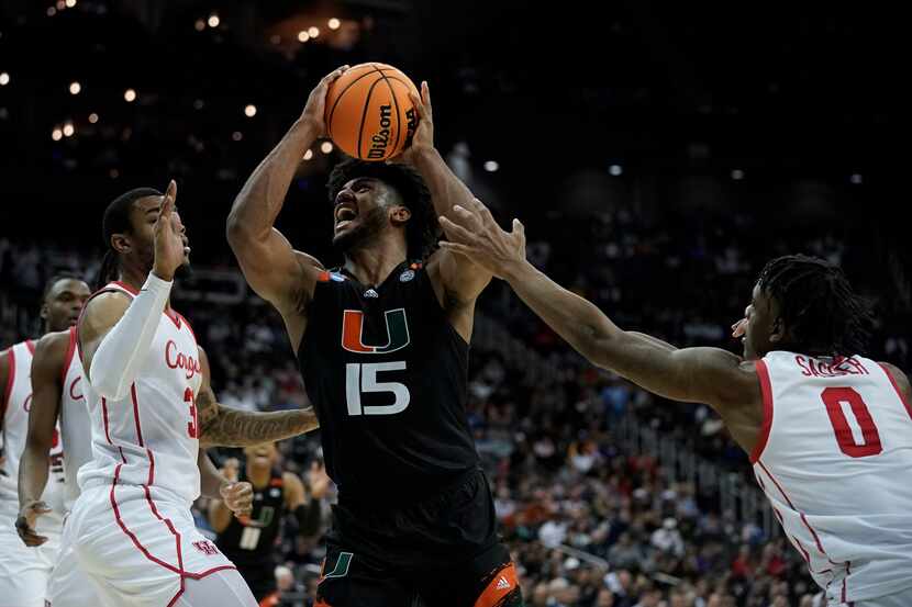 Miami forward Norchad Omier drives between Houston forward Reggie Chaney, left, and guard...