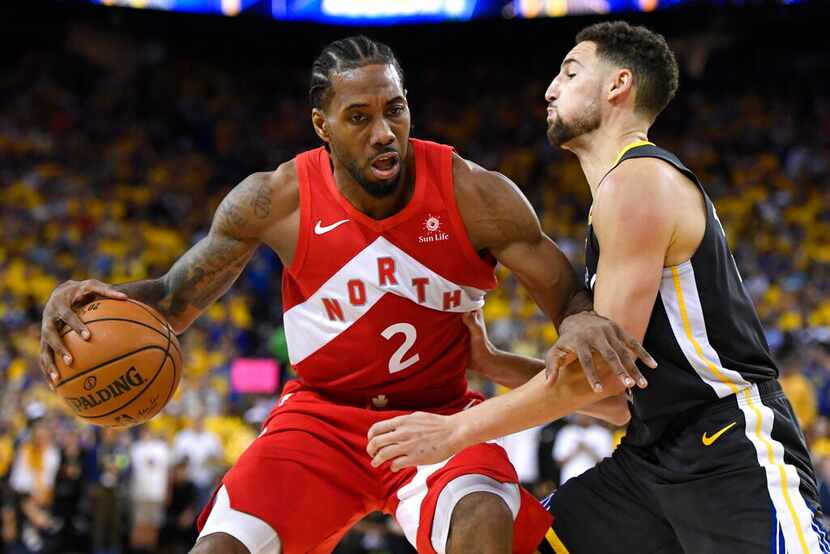 Kawhi Leonard, alero de los Raptors de Toronto, controla el balón delante de Klay Thompson,...