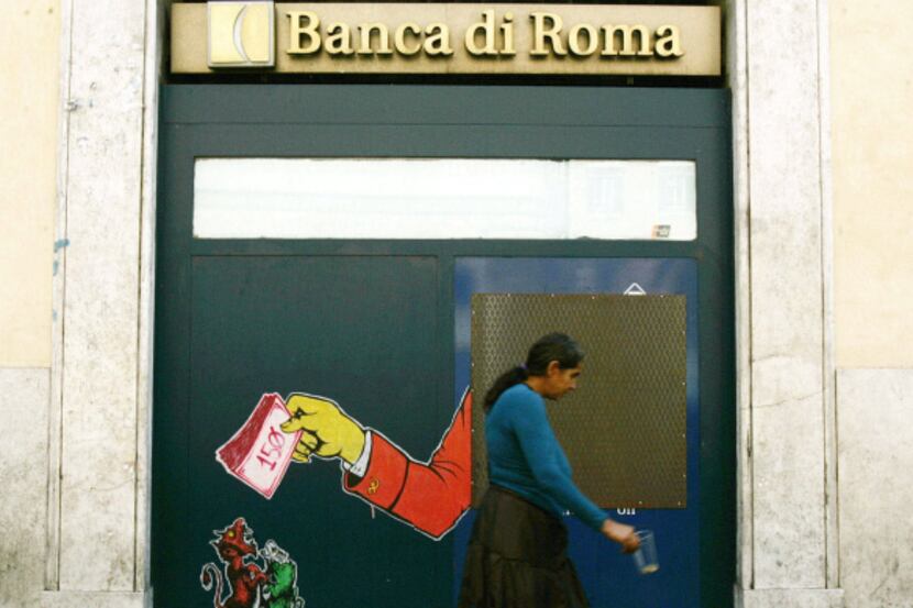 A woman who begs for money walks past a closed cash machine covered by graffiti in Rome.