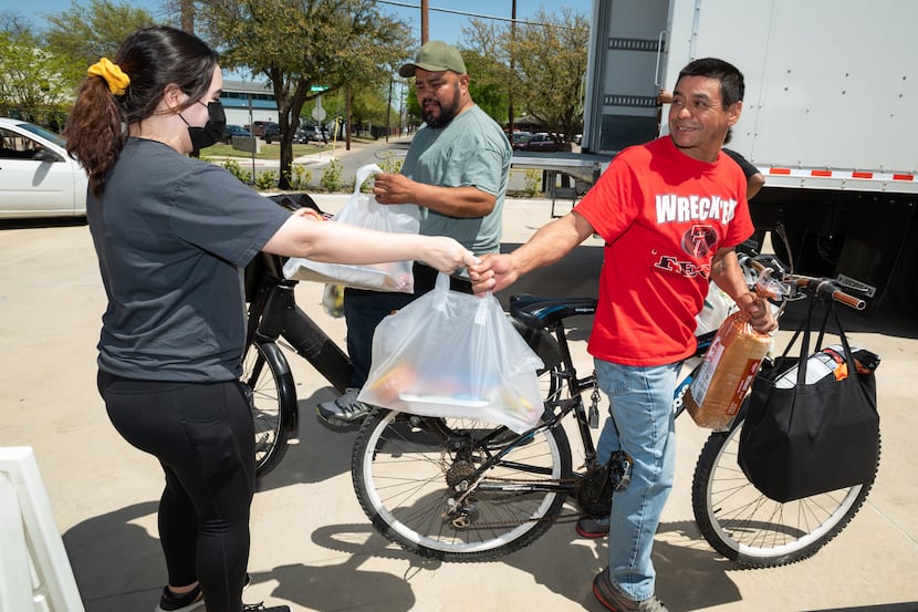 Goodr employee Gabriela Lopez, left, hands bags of food to Rocky Munoz, center, and his...