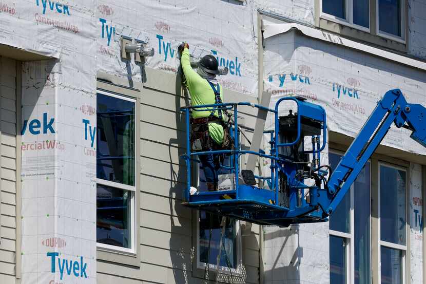 A construction worker uses a lift to work on the exterior of The Alexan Apartments along...