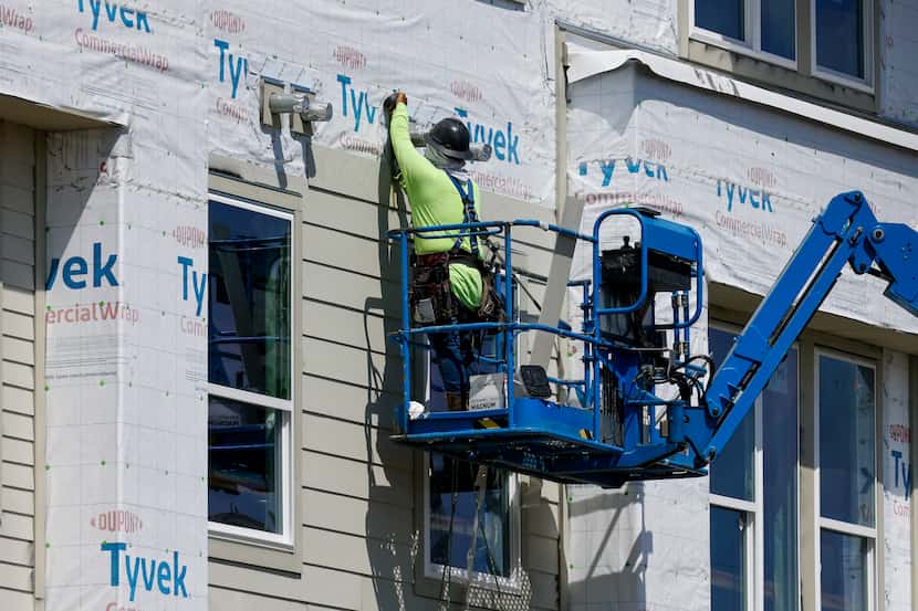 A construction worker uses a lift to work on the exterior of The Alexan Apartments along...
