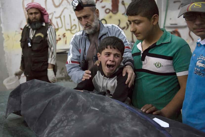 A Syrian boy is comforted as he cries next to the body of a relative who died in a reported...