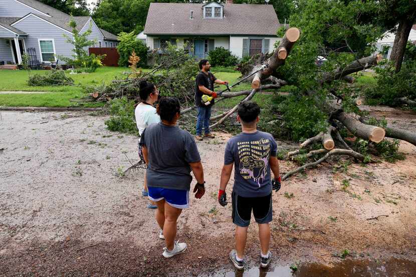 Carlos Porras uses a chainsaw to clear a fallen tree from the street outside his home as his...