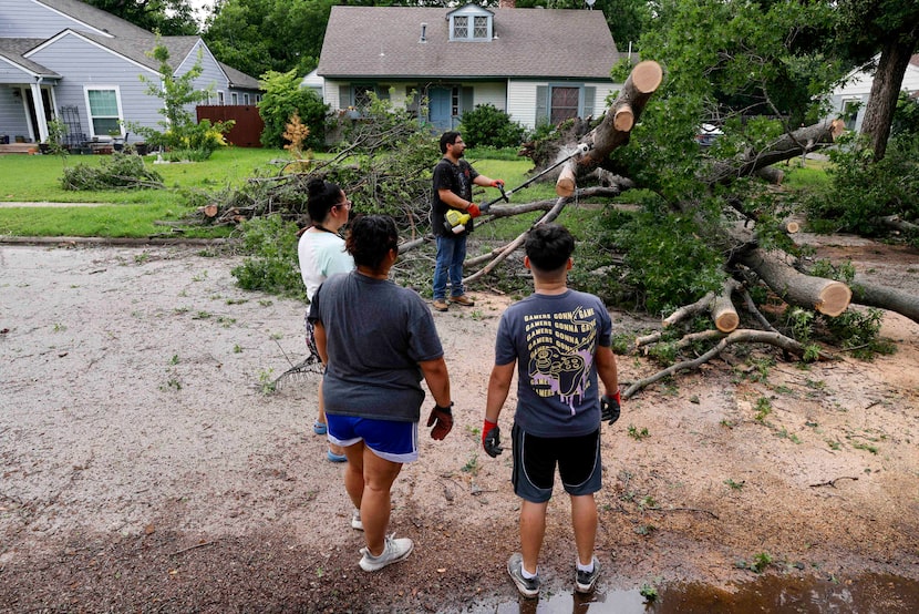 Carlos Porras uses a chainsaw to clear a fallen tree from the street outside his home as his...